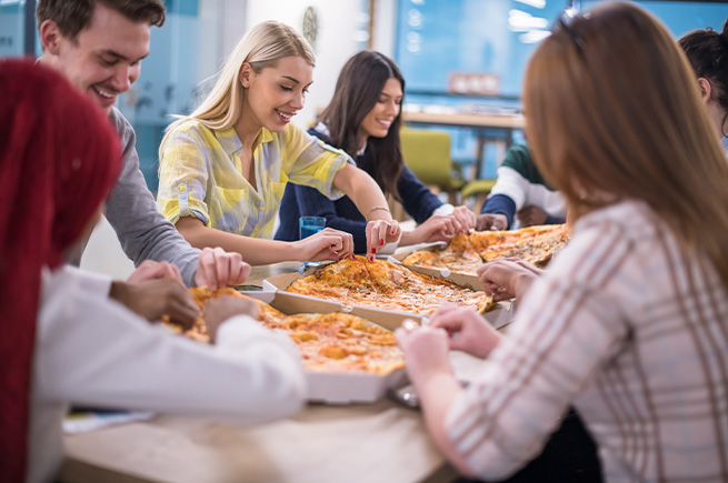 A group of office workers around a table eating pizza